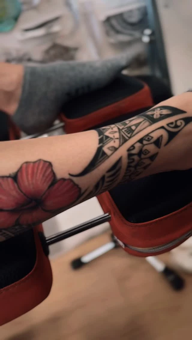 Tatouage polynésien sur l'avant-bras, accompagné d'un hibiscus rouge.
